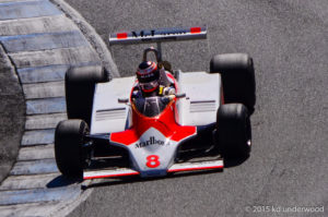 Red and white vintage race car on track.