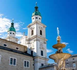 Church tower and fountain under blue sky.
