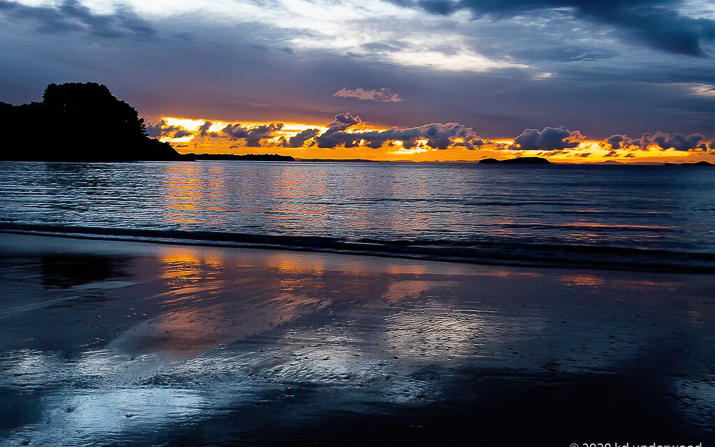 Sunset over ocean with reflective wet sand.